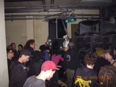 a group of people standing around in a room with speakers on the wall and one person wearing a red hat