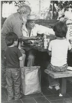 an old black and white photo of a man handing food to two children on a picnic table