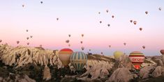 many hot air balloons are flying in the sky above some rocks and mountains at sunset