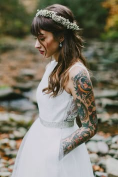 a woman in a white dress with tattoos on her arm and arms is standing next to a river