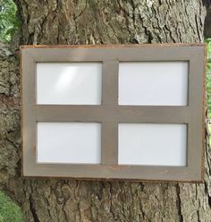 a wooden frame hanging on the side of a tree with four square white frames attached to it