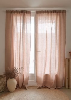 a living room with a round rug and two windows covered in pink drapes next to a plant