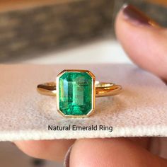 an emerald ring is being held by someone's hand