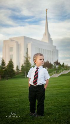 a young boy wearing a tie and standing in front of a large building with a steeple