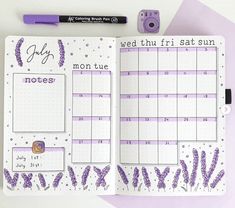 an open planner with purple flowers on it and a camera next to the calendar page