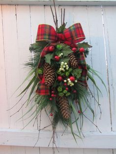 a wreath with pine cones, holly and berries hanging on the side of a door