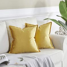 two yellow pillows sitting on top of a white couch next to a potted plant