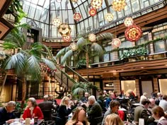 people sitting at tables in a restaurant with lots of lights hanging from the ceiling and palm trees