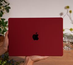 a person holding up an apple laptop in their left hand, on a wooden table