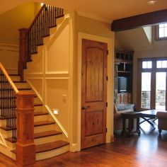 a living room filled with furniture next to a wooden stair case in front of a door