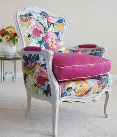 an old chair with floral fabric and pink cushion sits in the middle of a carpeted room