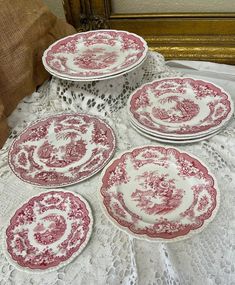 four red and white plates sitting on top of a lace covered tablecloth next to a pillow