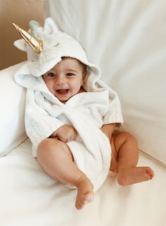 a baby wrapped in a unicorn towel sitting on a bed