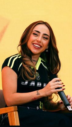 a woman sitting in a chair holding a microphone and smiling at the camera while wearing a black shirt