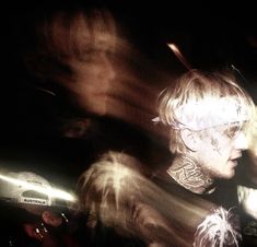 a man with white hair and piercings on his neck standing in front of a group of people