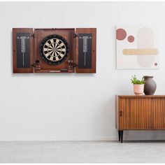 a dart board mounted to the side of a wall next to a wooden cabinet with two vases on it