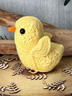 a yellow knitted bird sitting on top of a wooden table next to a branch