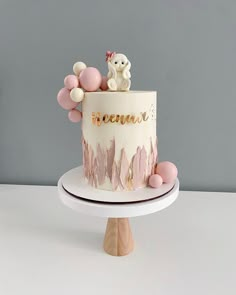 a white cake with pink frosting and balloons on top is sitting on a stand