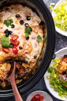 a crock pot filled with taco salad and topped with black olives, cilantro, red pepper, green onion, and cheese