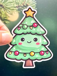 a hand holding up a green christmas tree sticker