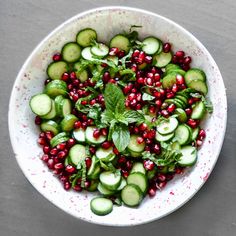 a white bowl filled with cucumbers, pomegranates and leaves