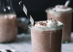 two glasses filled with chocolate milkshakes and topped with whipped cream on a table