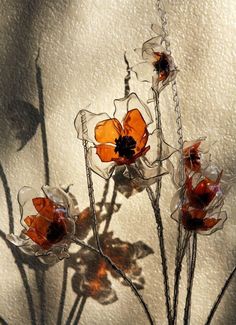 three glass flowers with long stems in front of a white wall