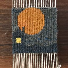 a close up of a weaving machine on a wooden table with an orange and black design