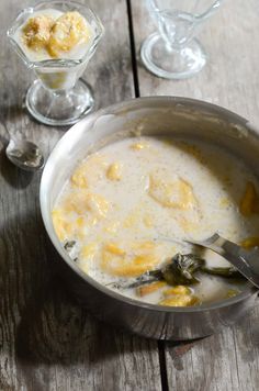 a silver bowl filled with soup next to two glasses on top of a wooden table