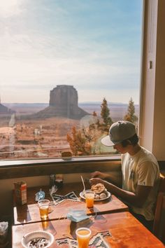 a man sitting at a table in front of a window with food and drinks on it