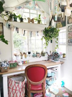 a room filled with lots of plants next to a window and a red chair in front of a counter