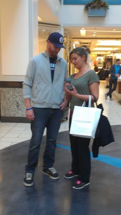 a man standing next to a woman in a mall holding shopping bags and looking at her cell phone