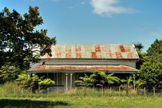 an old run down house in the middle of a field with trees and bushes around it