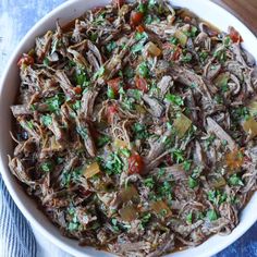 a white bowl filled with shredded meat and garnished with parsley on top