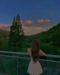 a woman standing on top of a balcony next to a lush green forest covered hillside