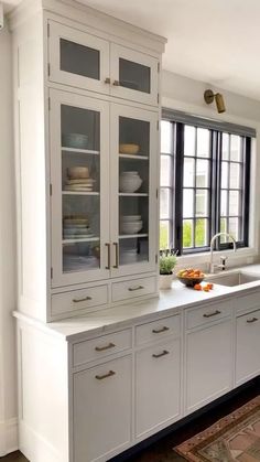 a kitchen with white cabinets and windows in the wall, along with a rug on the floor