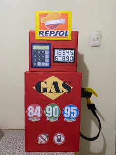 a vending machine that is red and yellow with gas prices on the front, sitting next to a white wall