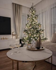 a living room with a christmas tree in the corner and two wine glasses on the coffee table