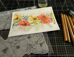 some pencils and markers are sitting on a table next to an envelope with flowers painted on it