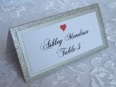 a table name card with a red heart on the top and silver glittered border