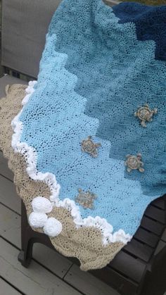 a crocheted blanket is sitting on a bench with shells and seashells