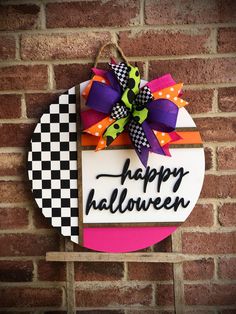 a sign that says happy halloween hanging on a brick wall with a checkered bow