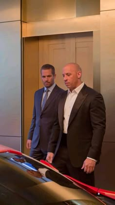 two men in suits standing next to a car