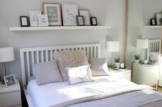 a white bed topped with pillows next to two framed pictures on the wall above it