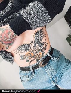 a woman with tattoos on her stomach and arm is wearing blue denim shorts, a black sweater and a rose tattoo