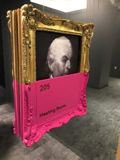 a pink and gold frame with an old man's face on it in front of a black wall