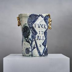 a ceramic vase sitting on top of a white block with gold chains around the edges