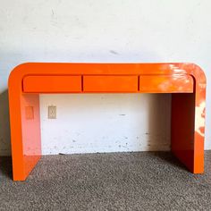 an orange desk sitting on top of a carpeted floor next to a white wall