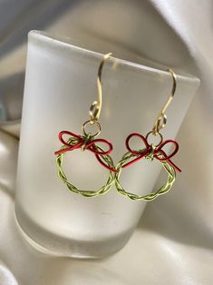 red, green and gold earrings with bows on them sitting on a white glass cup