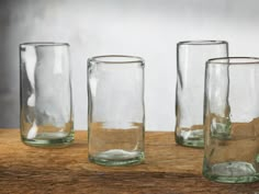 four glasses sitting on top of a wooden table next to each other with water in them